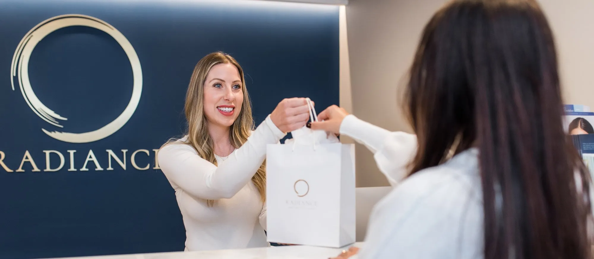 front desk helping a customer with a bag of facial products. Contact Radiance Medical Spa for your skincare needs.